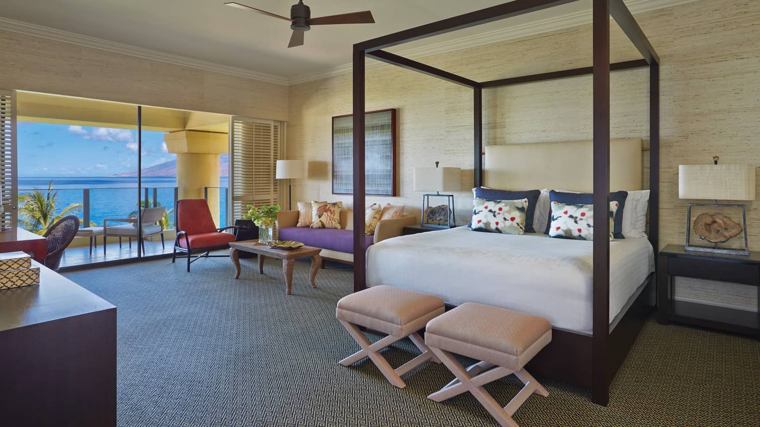 Luxury bedroom with a four-poster bed, seating area and ocean-view balcony at a tropical resort suite