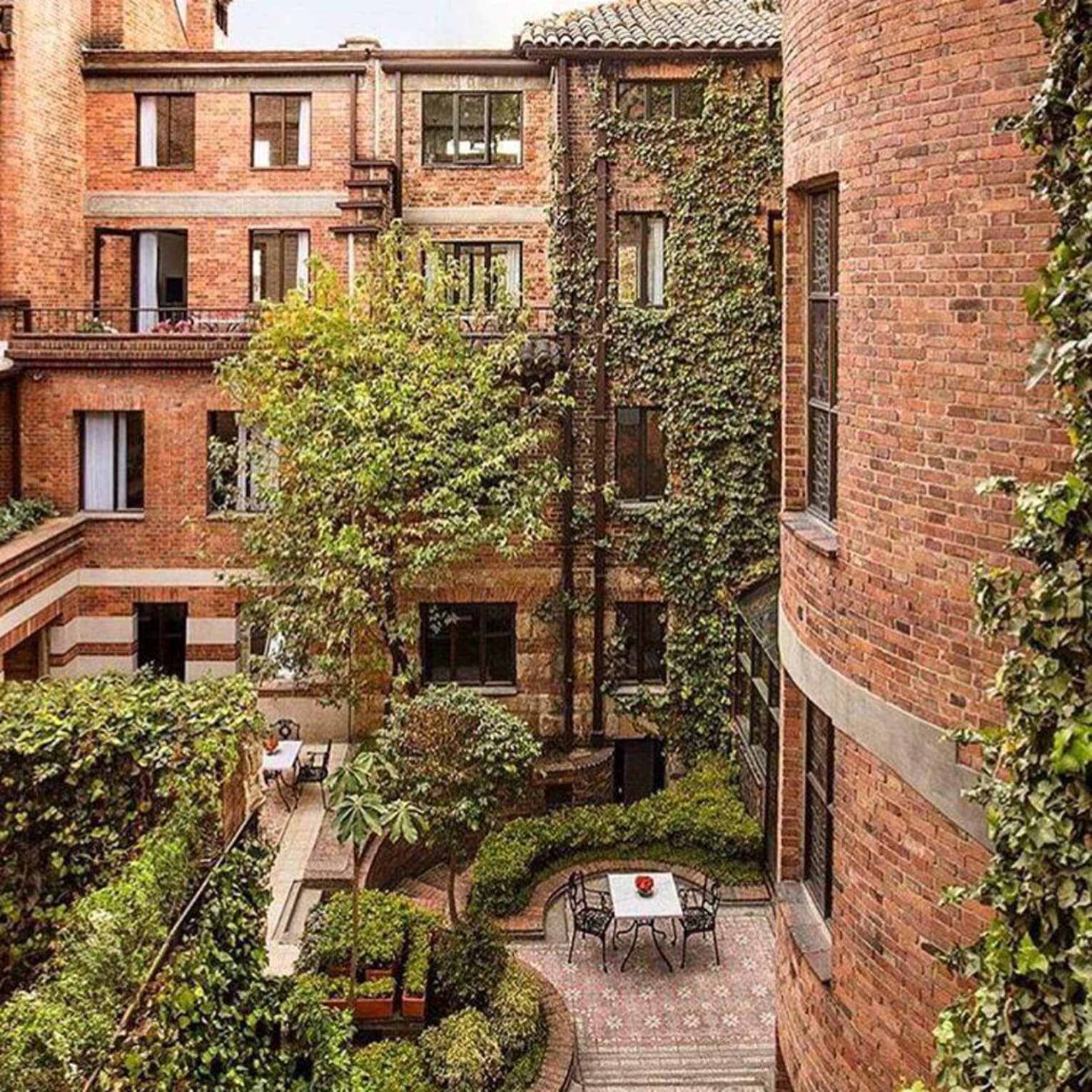 Looking down at courtyard patio surrounded by brick building, windows, green trees, shrubs 