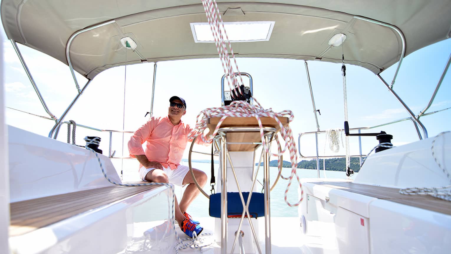 Smiling man sits on bench behind ropes in white sailboat