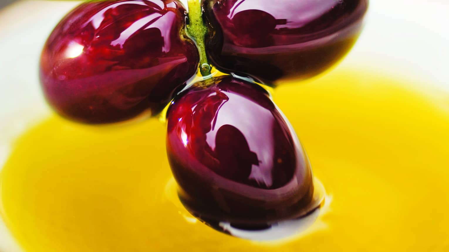 Close-up of three shiny purple olives on vine over yellow sauce