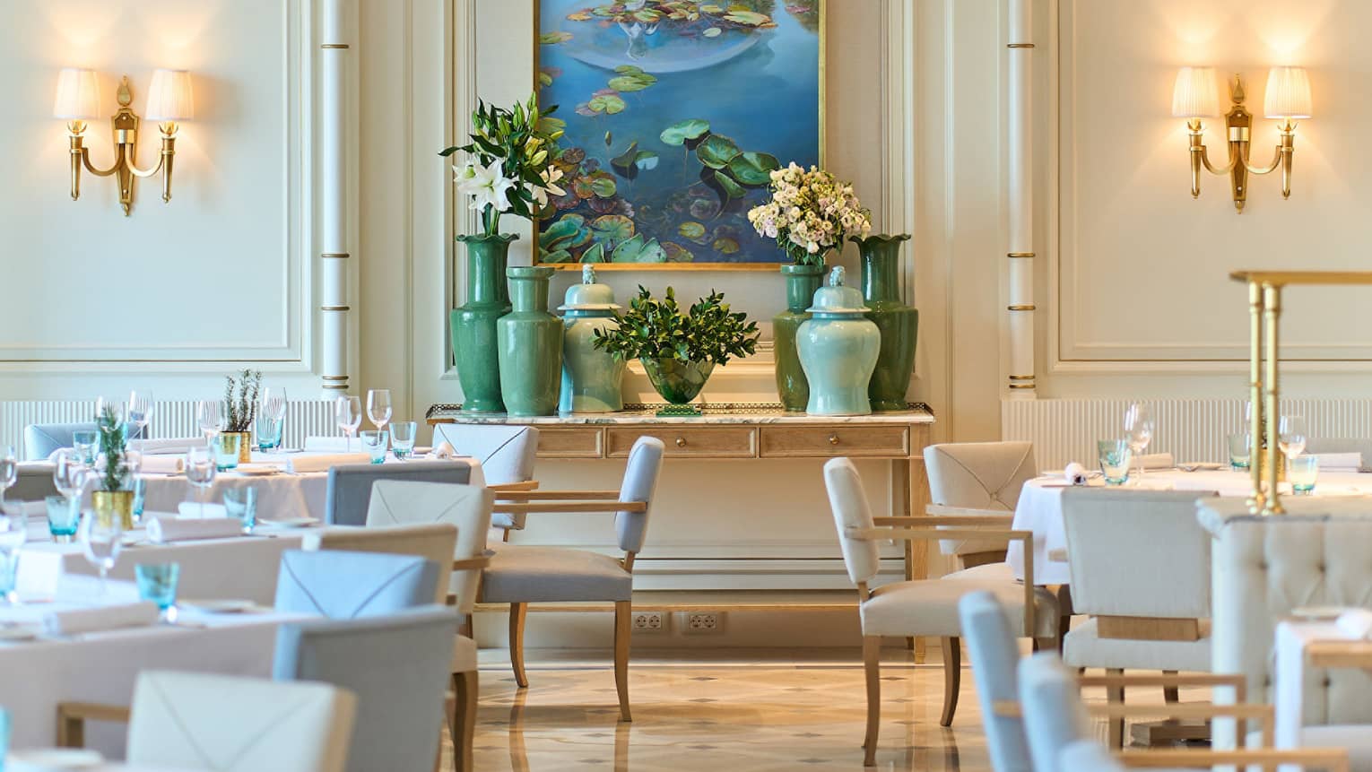 Brightly lit dining room of Riviera with lighted wall sconces, pale blue and white chairs, shiny patterned floor