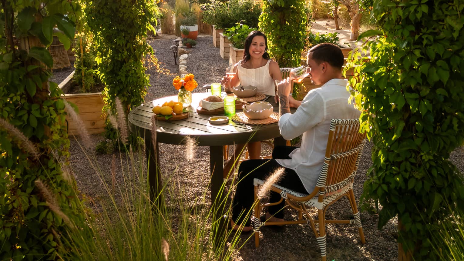 Two people at a small outdoor dining table in an outdoor space surrounded by lush greenery