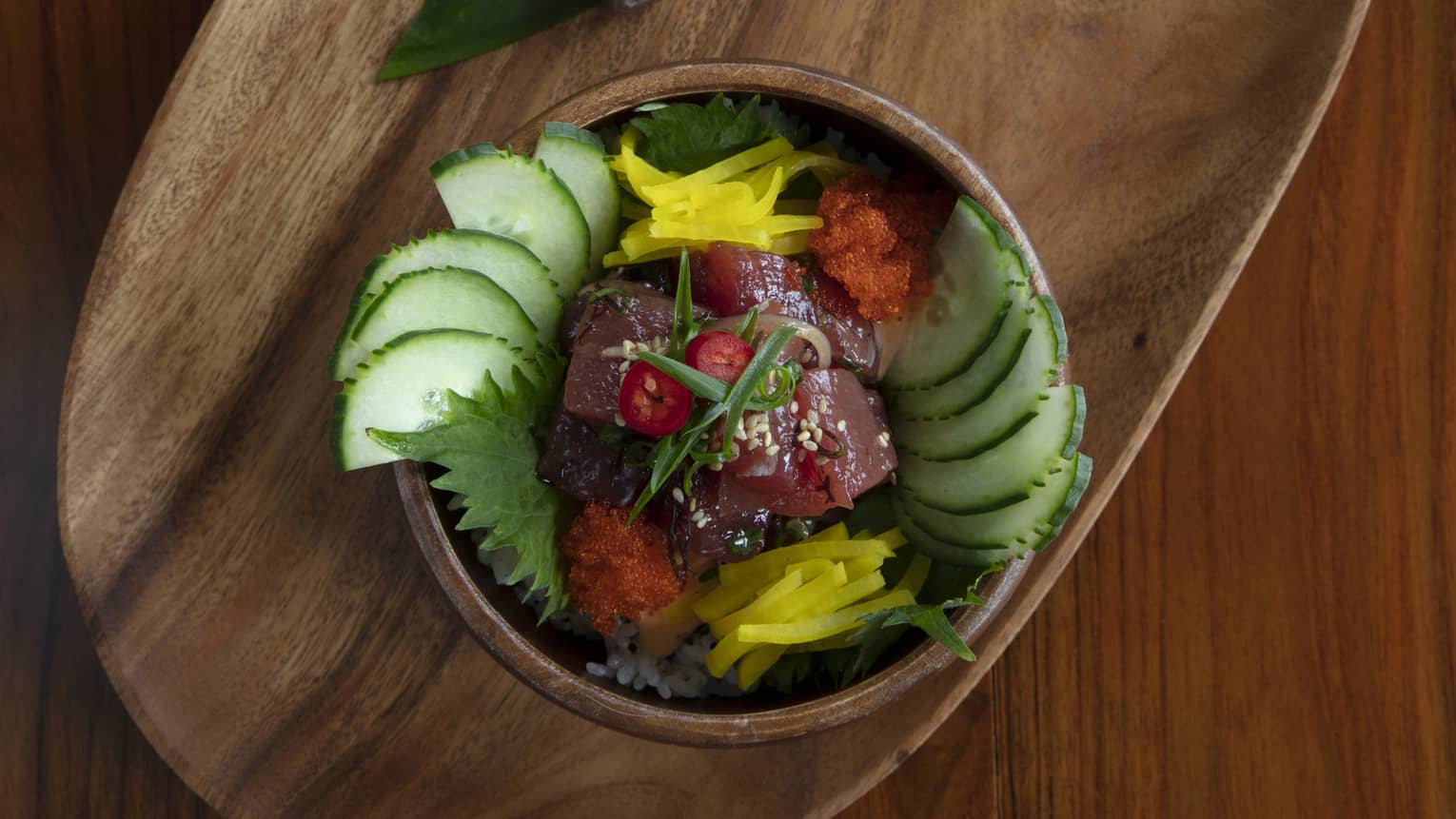 Aerial shot of ahi tuna poke bowl with cucumber and pickled daikon garnishes on an oblong wooden plate