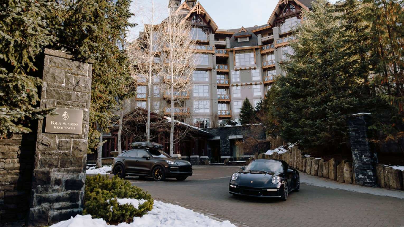 Two black Porsches parked in brick drive in front of towering Four Seasons property