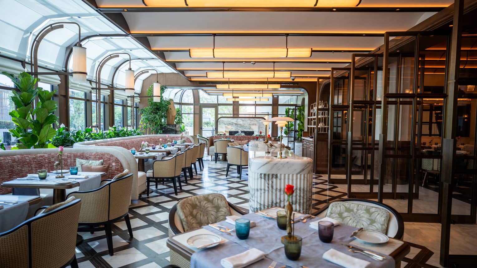 Indoor restaurant with tables of four and booths, black and white tiled floor, plants and overhead lighting