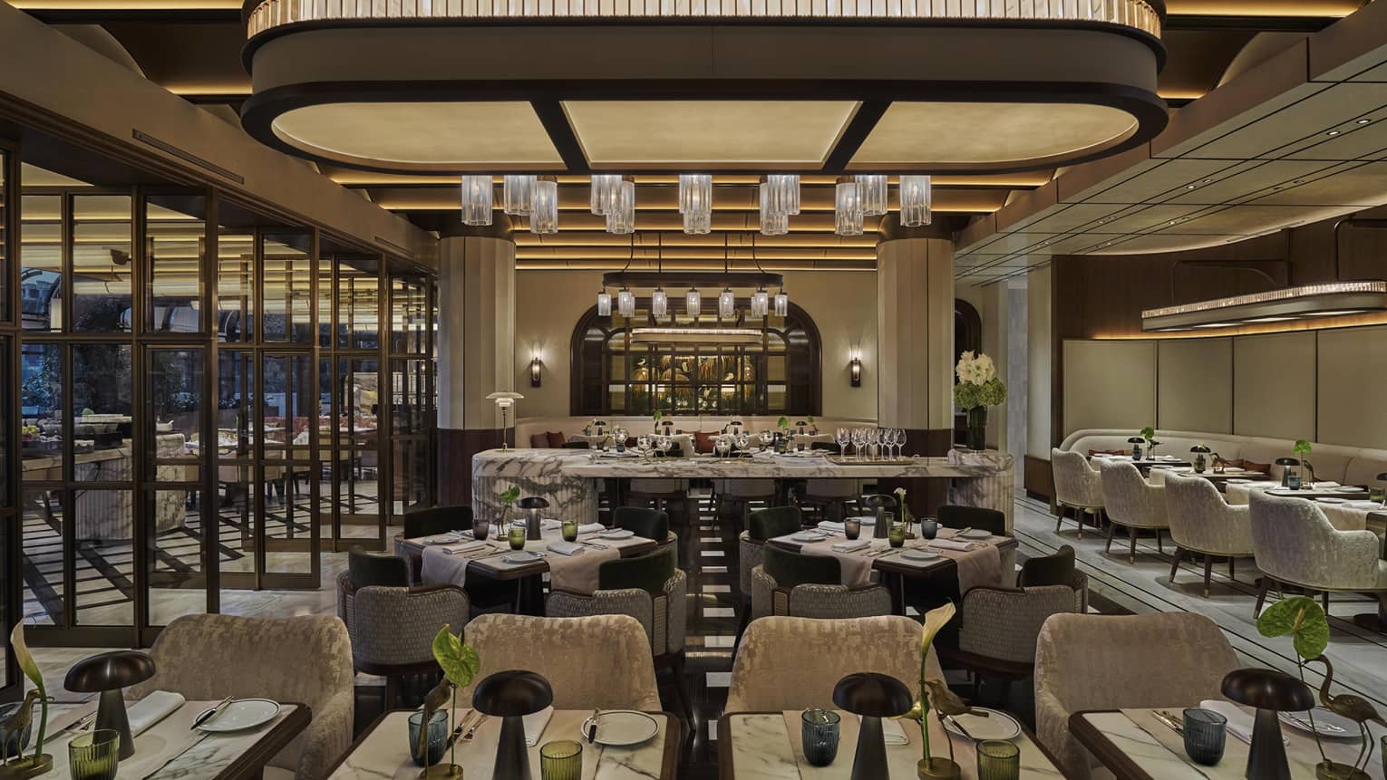 Restaurant dining room with grey and cream colour palatte, green florals on every table and a large overhead curved light piece