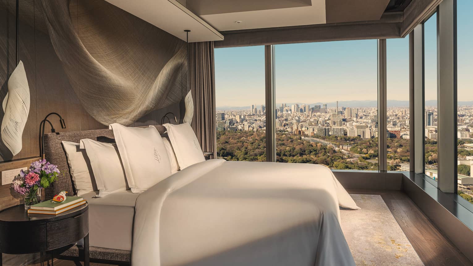 Luxury hotel room with a king bed, modern hanging lighting fixtures, and two walls of windows