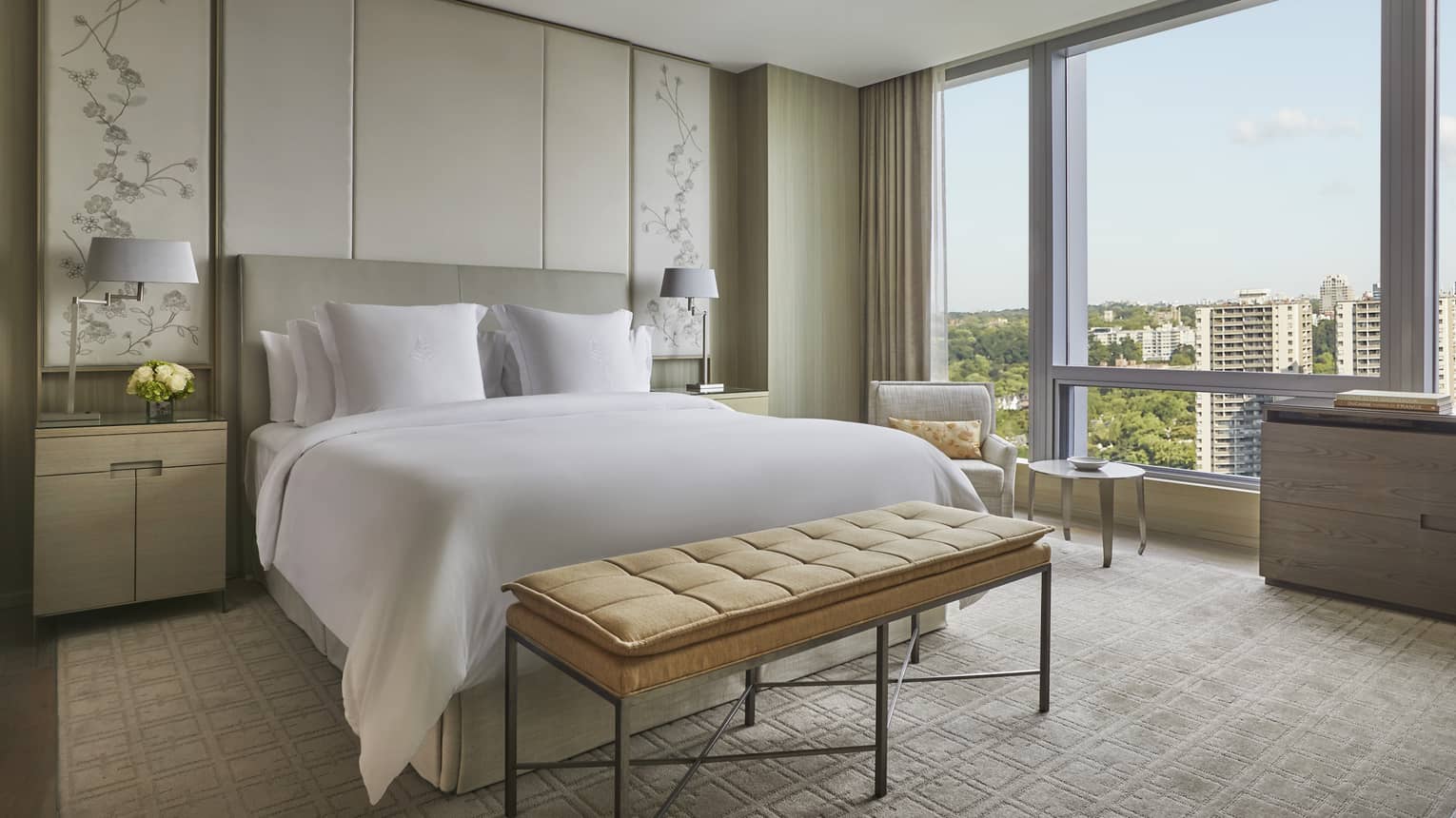 Guest room with white King bed, gold foot-of-the-bed bench, corner armchair and table, floor-to-ceiling window with views of downtown Toronto