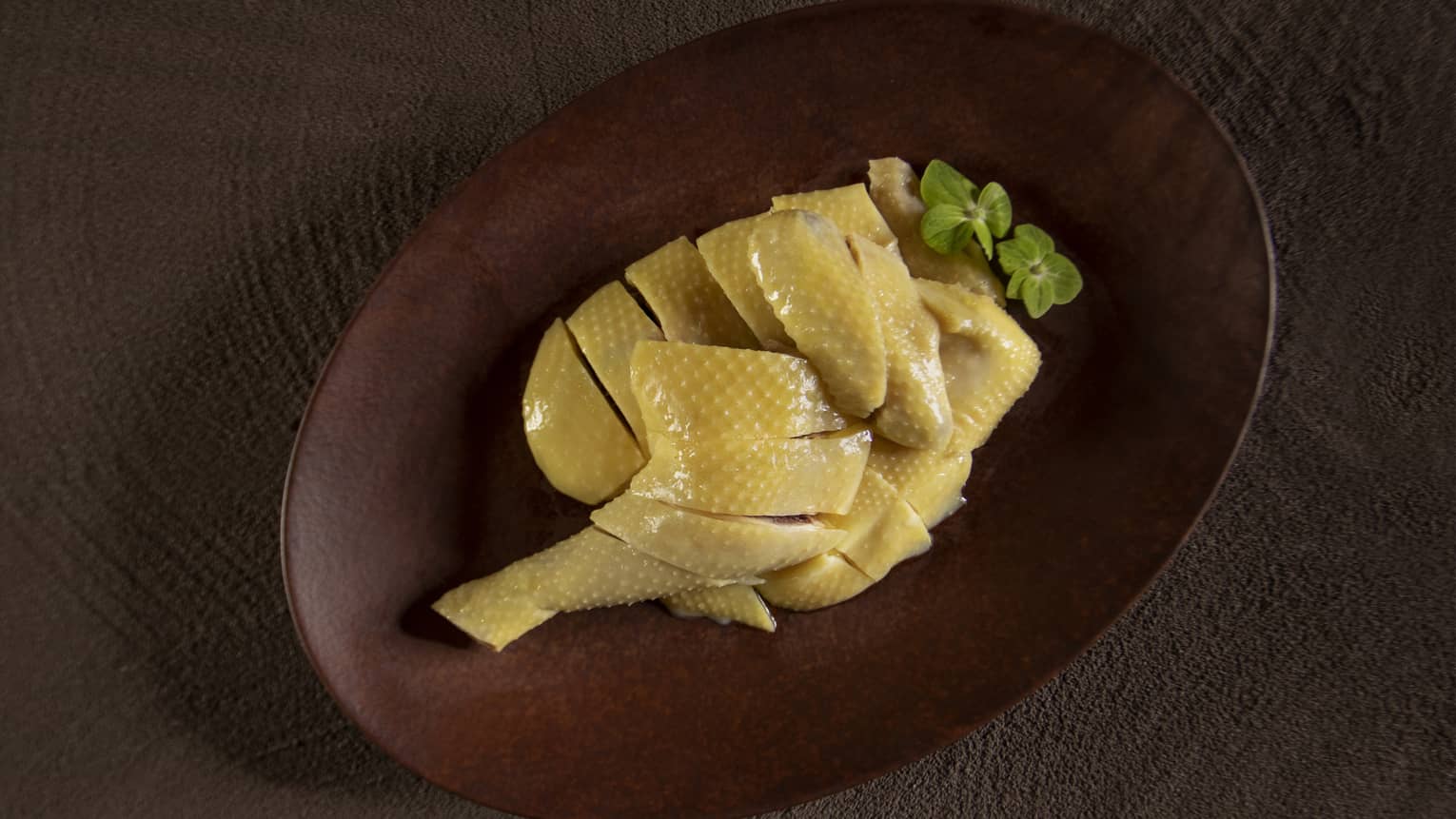 Poached chicken leg quarter in oval wooden dish with green flower garnish