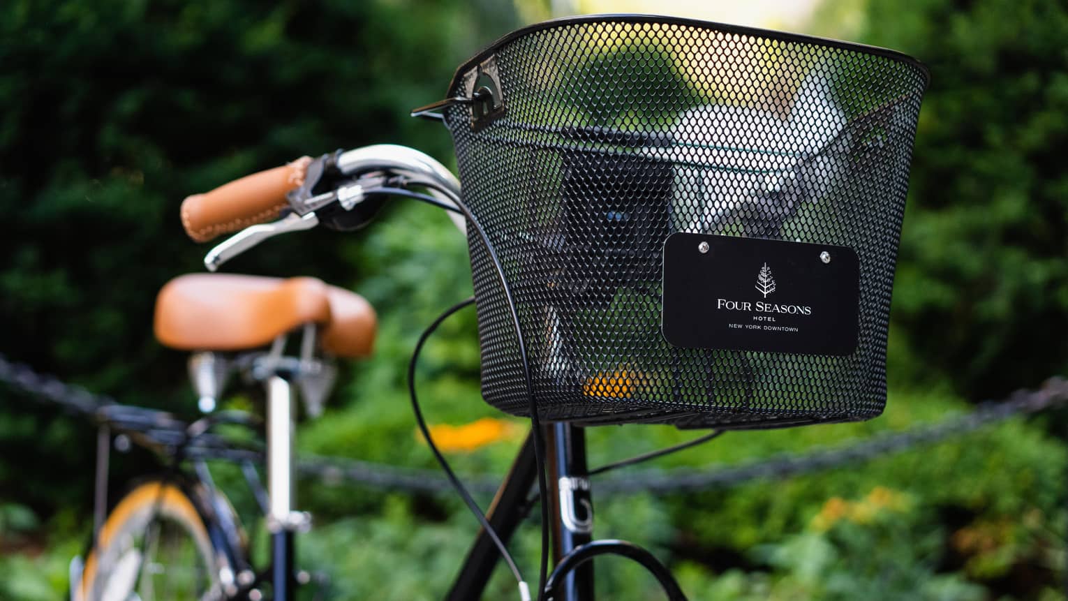 A bike with a black basket at the front that says "Four Seasons" outside by plants.