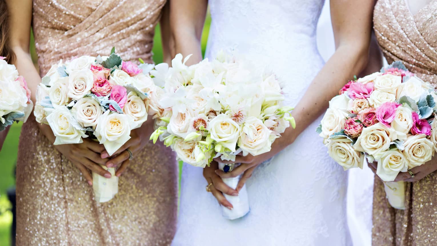 Bride and two bridesmaids in shimmering dresses hold white rose floral bouquets