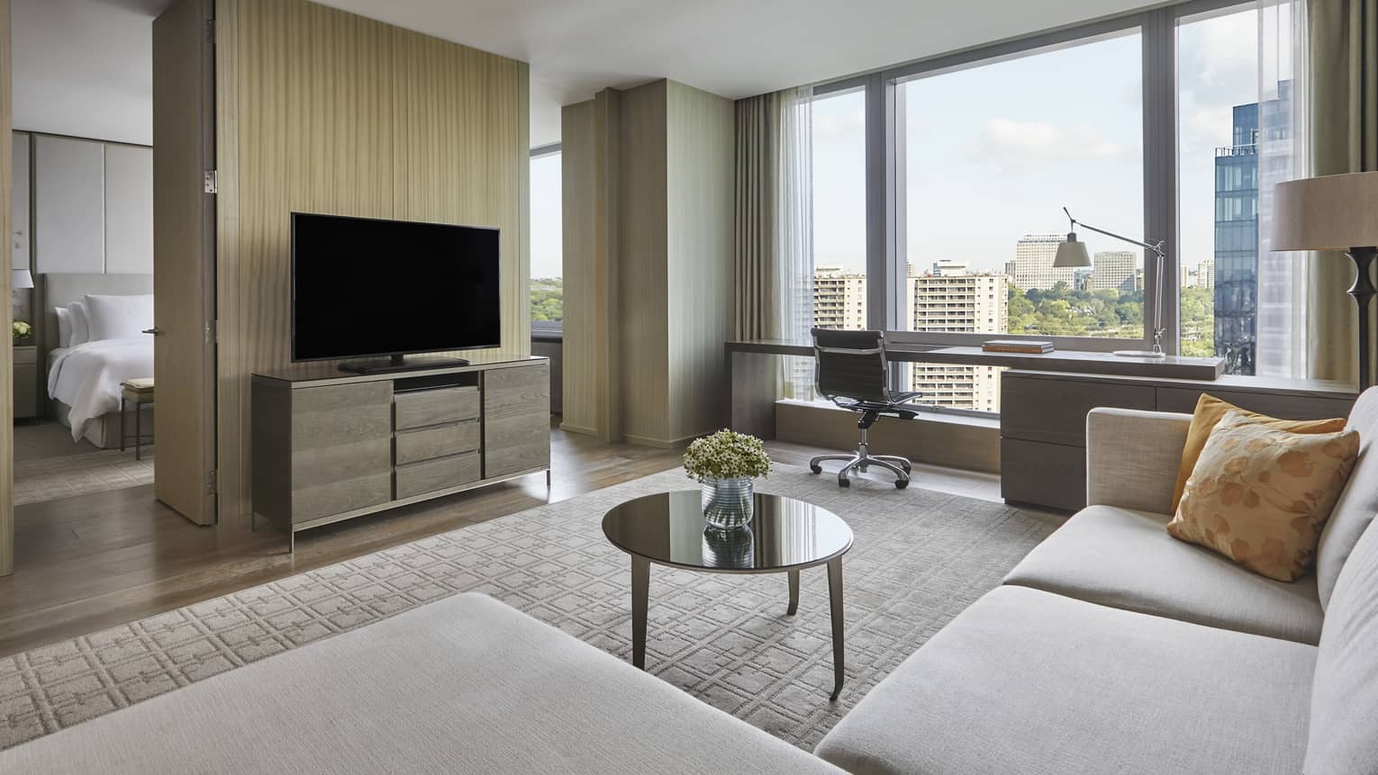Living room with a sofa, coffee table, and a tv set against a partial wall that opens to the bedroom