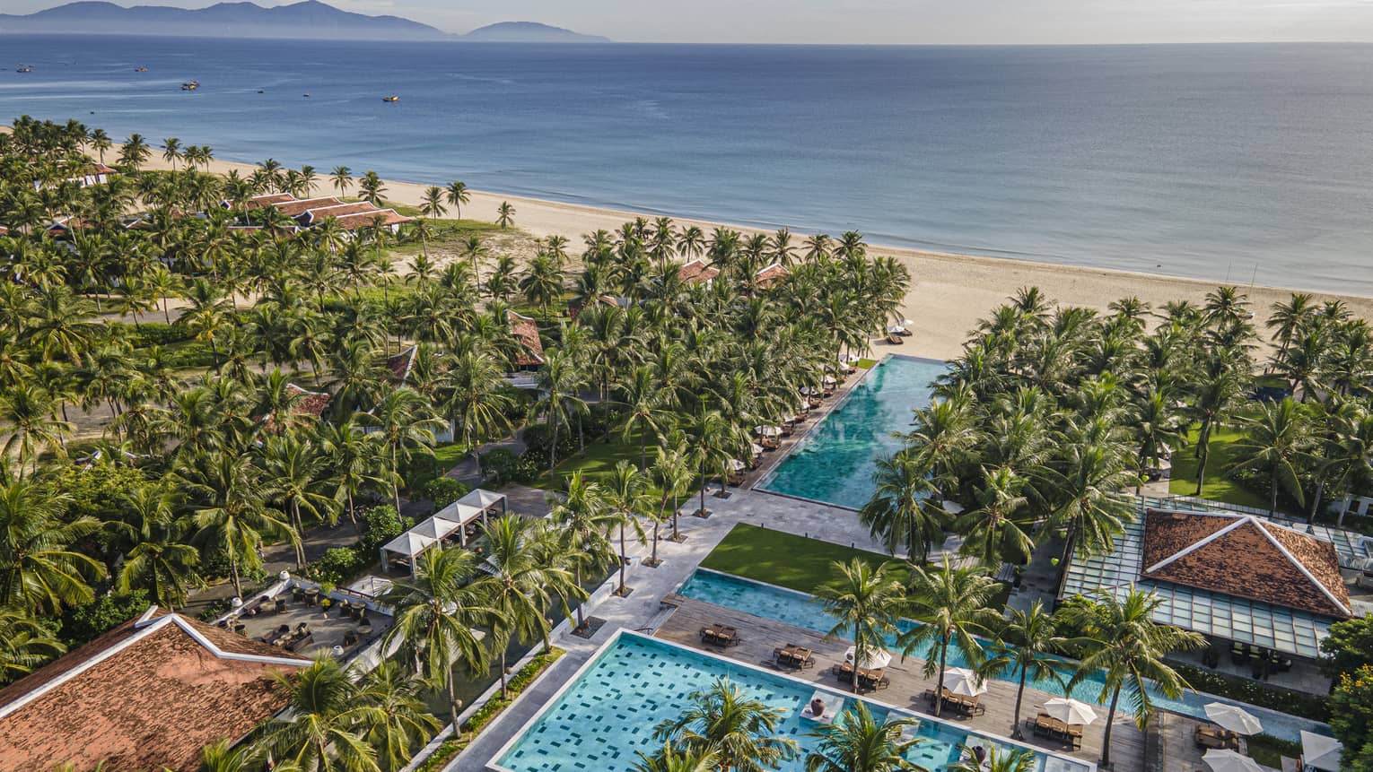 Aerial view of the resort pools with ocean views, palm trees and blue skies