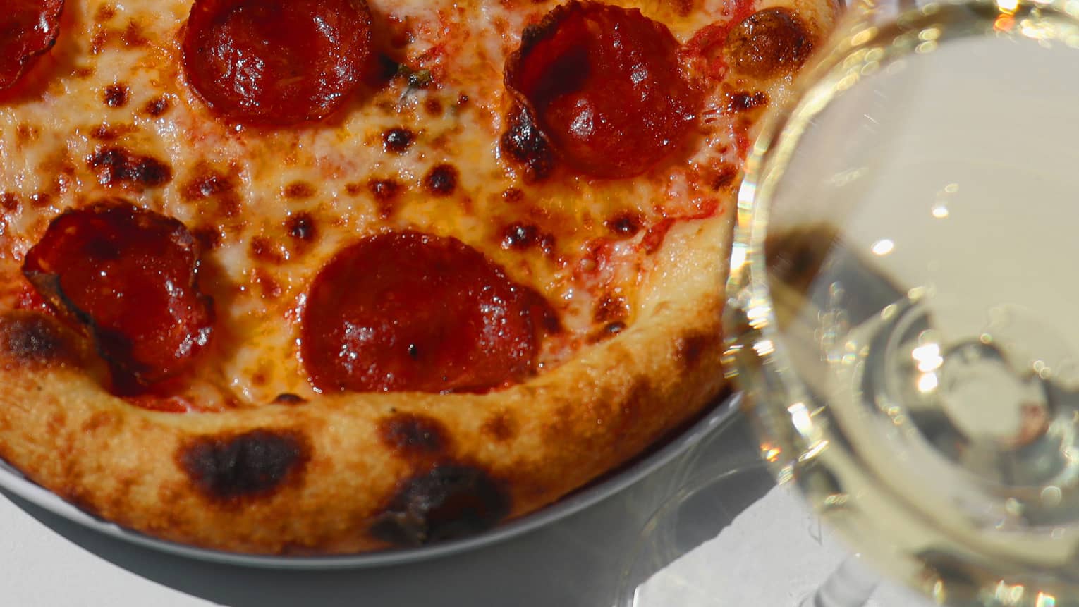 A pizza with pepperoni next to a glass of wine.