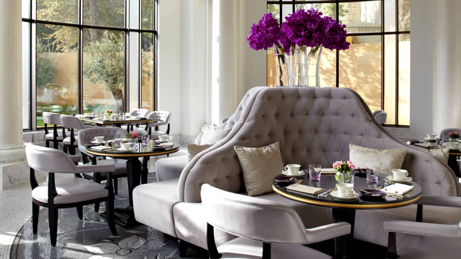 Sunny Zafferano dining room with tall, curved plush grey banquettes with purple flowers in vase above, chairs