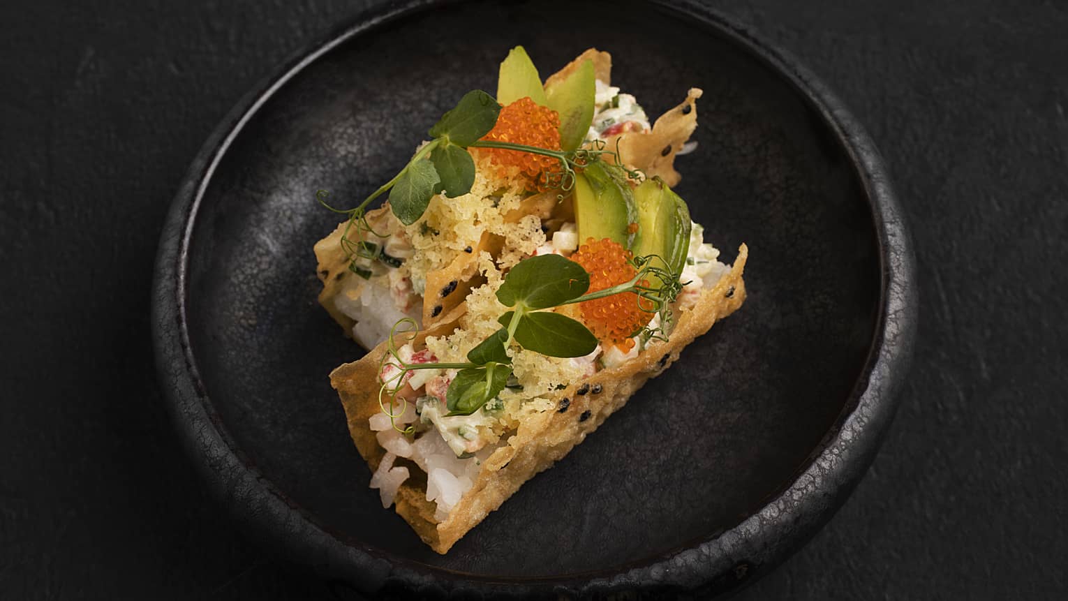 Two crispy shells filled with crab stick, cucumber, avocado, orange tobiko, tempura flakes and wasabi mayonnaise served on a black round plate