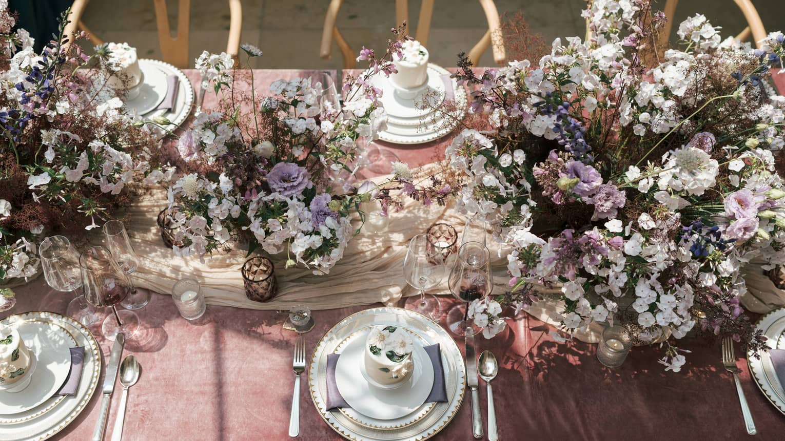 A table with white, purple and pink flowers, white plates and wood chairs.