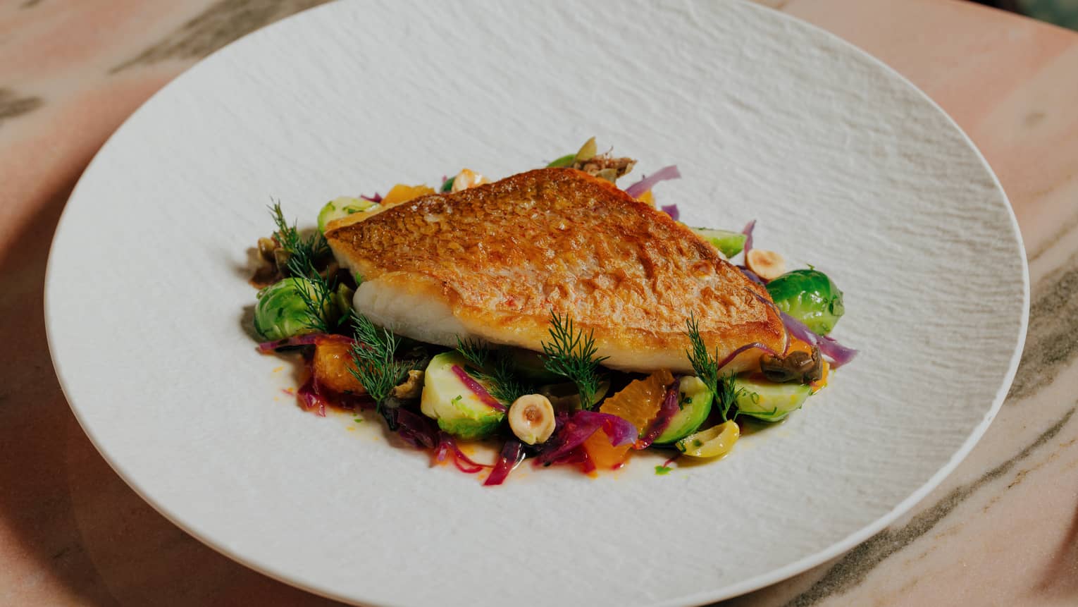 Snapper served with Brussels Sprouts Fricass�e, Caper, Parsley, Mandarin, Green Olive Hazelnut and Vierge Sauce on w white plate