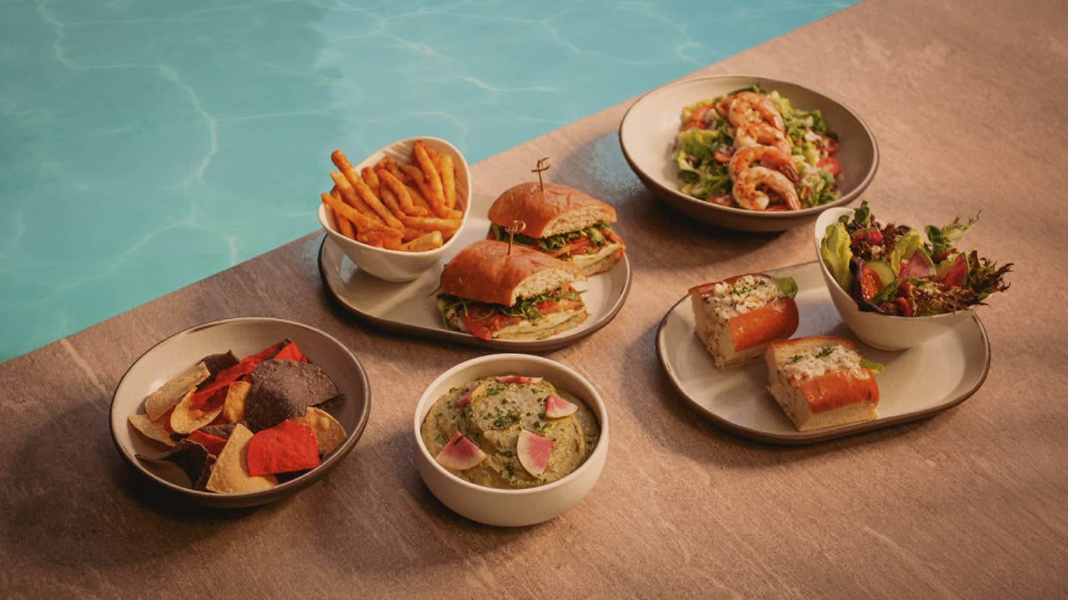Burgers, fries and other food in plates set next to pool