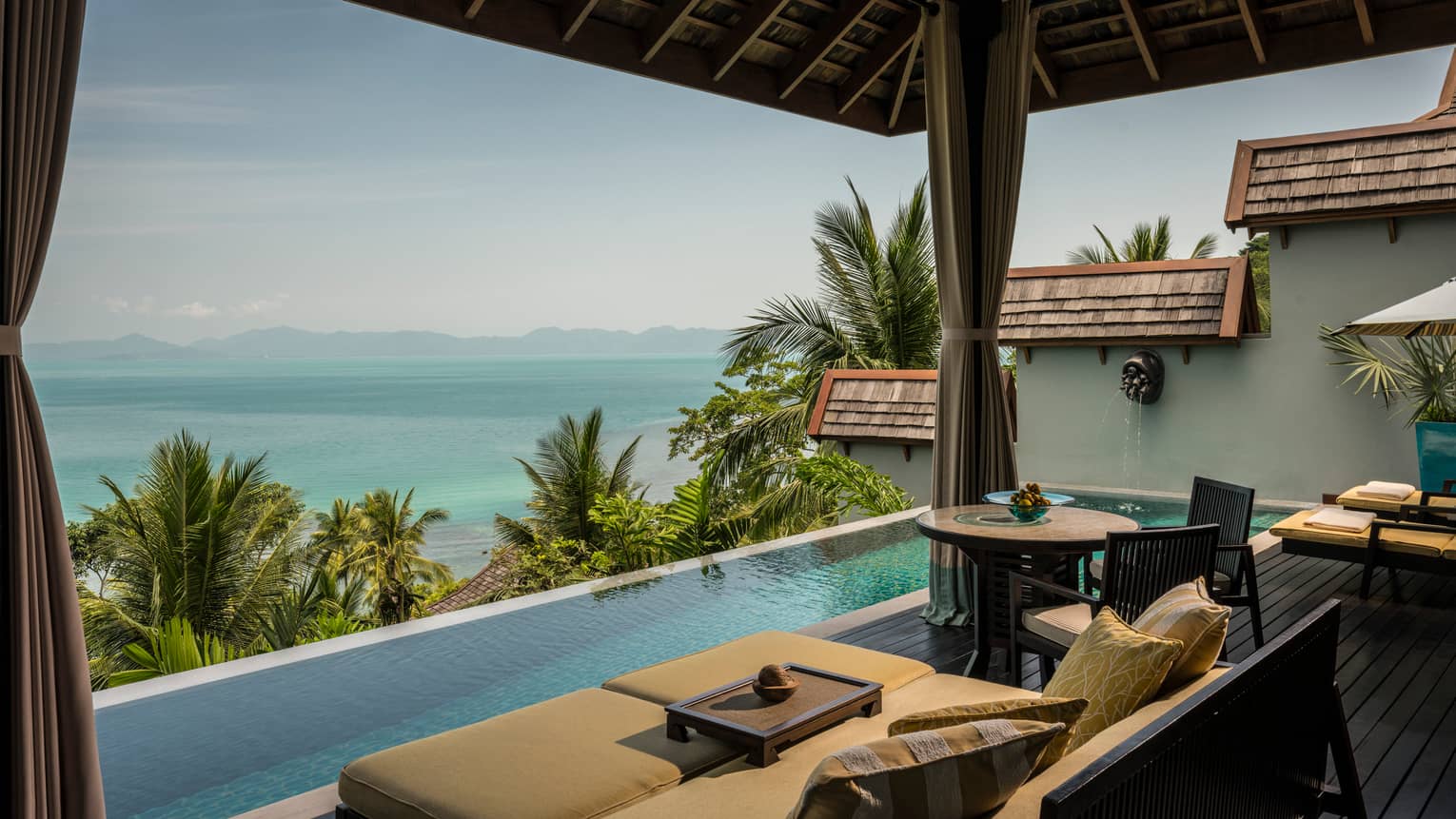 Patio chairs, cushions by infinity swimming pool on villa deck