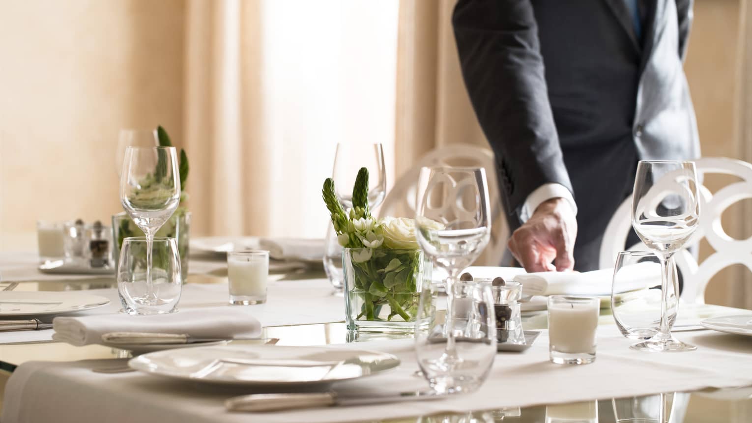 Hotel staff places napkin on small, elegant dining table in sunny room