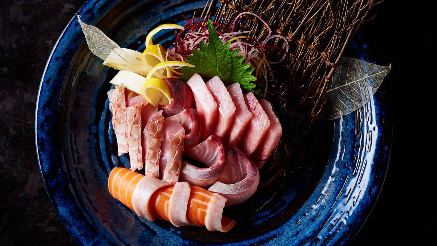 Slices of raw fish sashimi, seaweed, pickled ginger arranged on plate