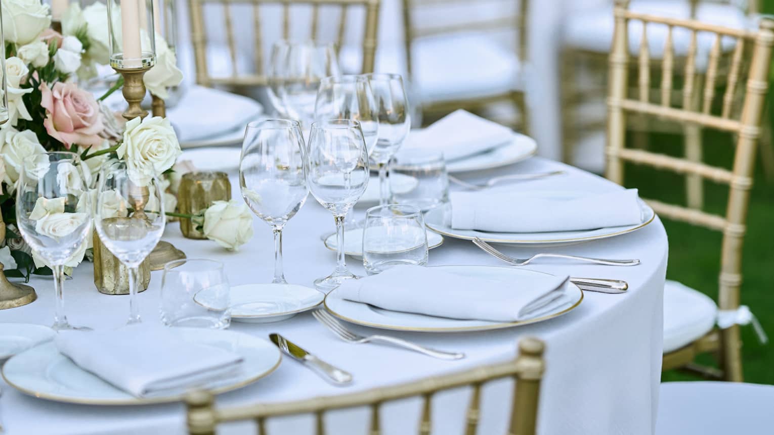 Outdoor banquet tables decorated with white floral bouquets, candles, and elegant glassware
