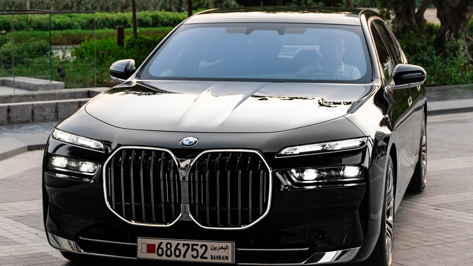 A black sports car parked on a path lined with lush green trees and hedges