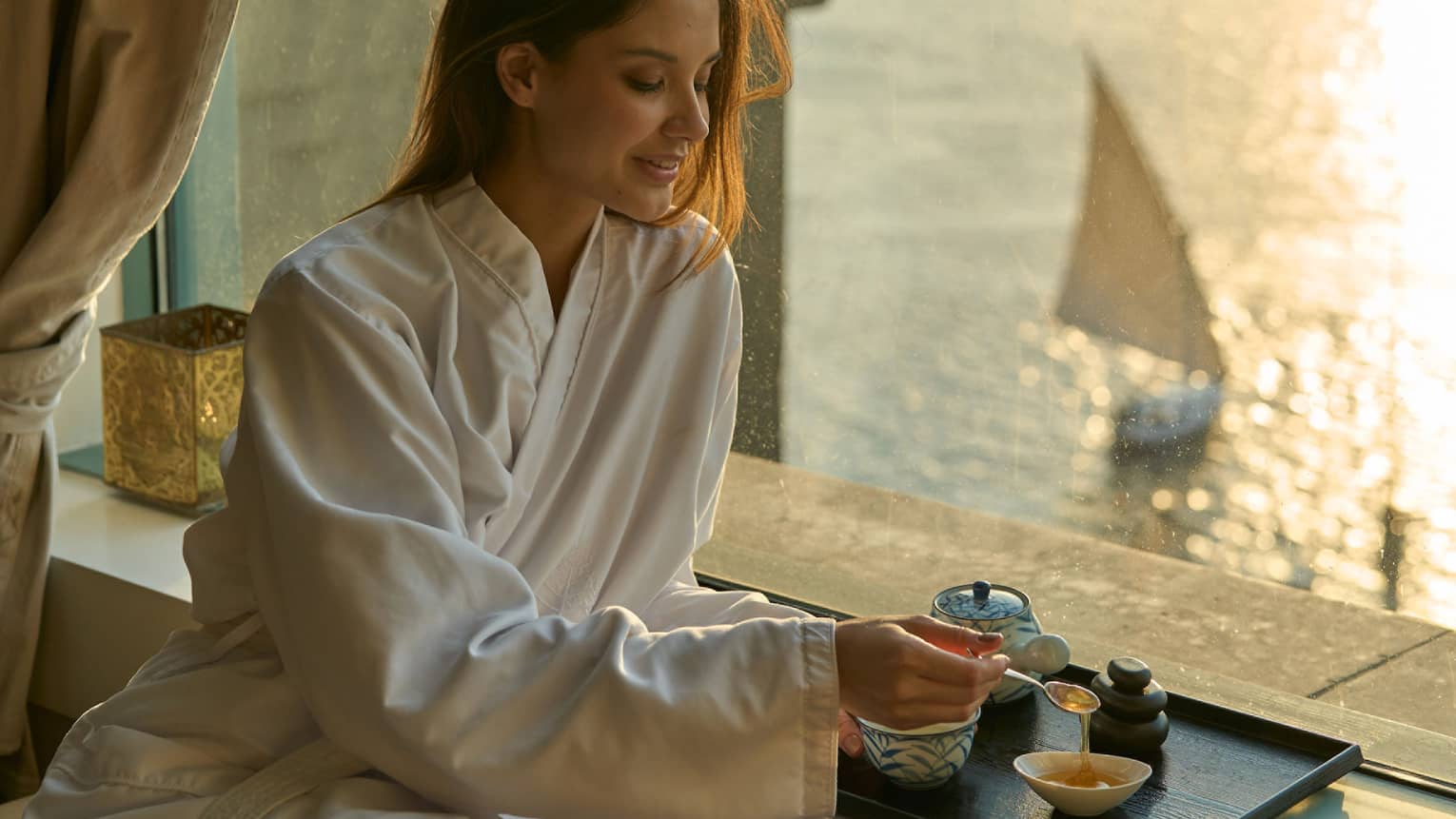 Woman in Four Seasons robe enjoys tea by the window at sunset