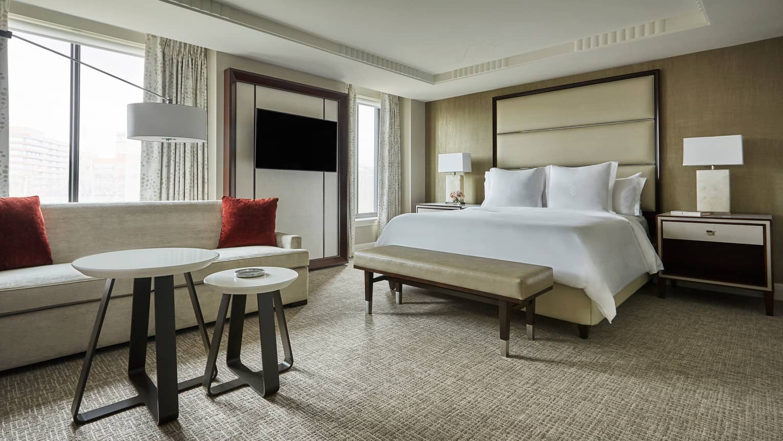 Grand Premier Room sofa with red accent pillows, tables in front of bench, bed, tall padded headboard beside picture windows