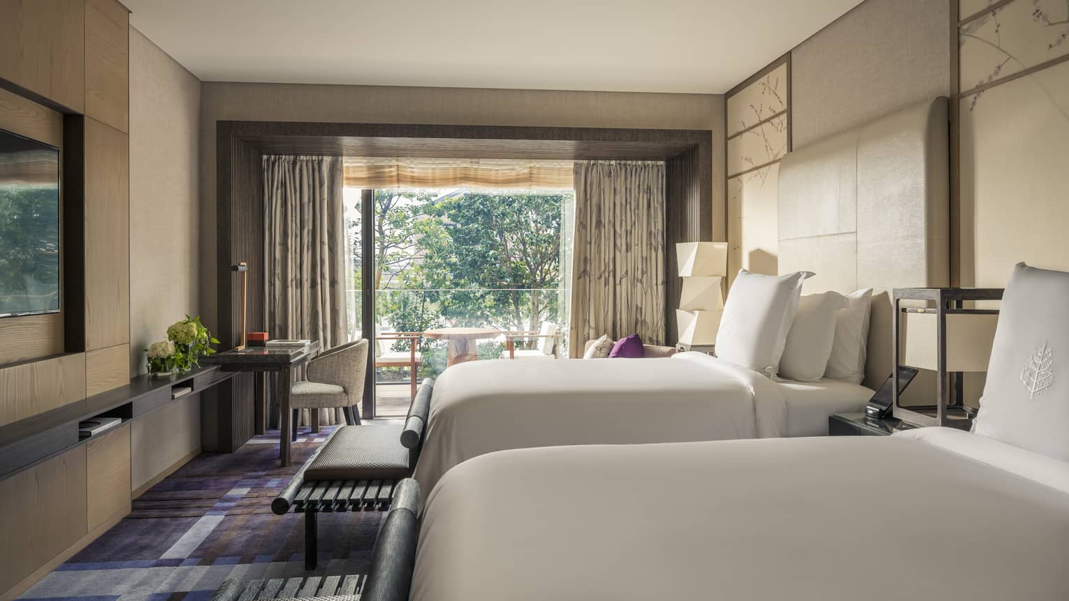 Hotel room with two beds, a work desk and a private balcony with outdoor seating and garden view