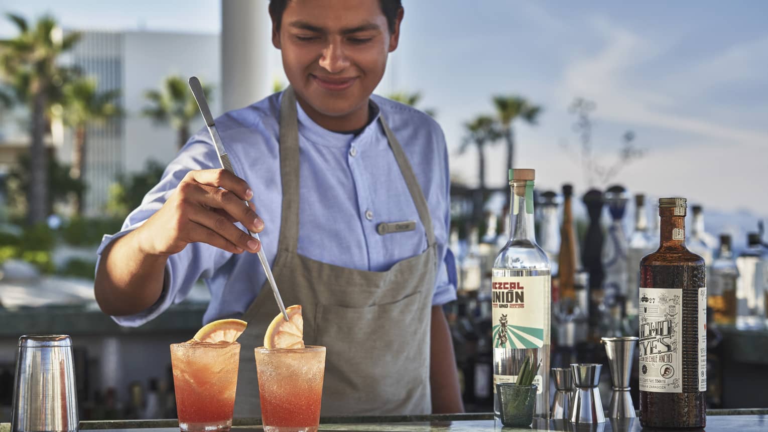 A Casa de Brasa mixologist garnishes two pink cocktails with a slice of citrus at an our door bar 