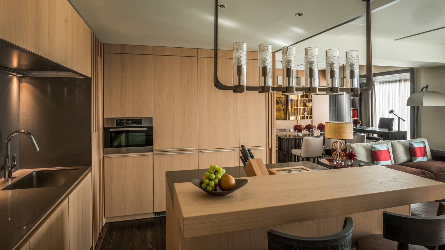 Corner of kitchen with light wood floor-to-ceiling cabinets, island under chandelier