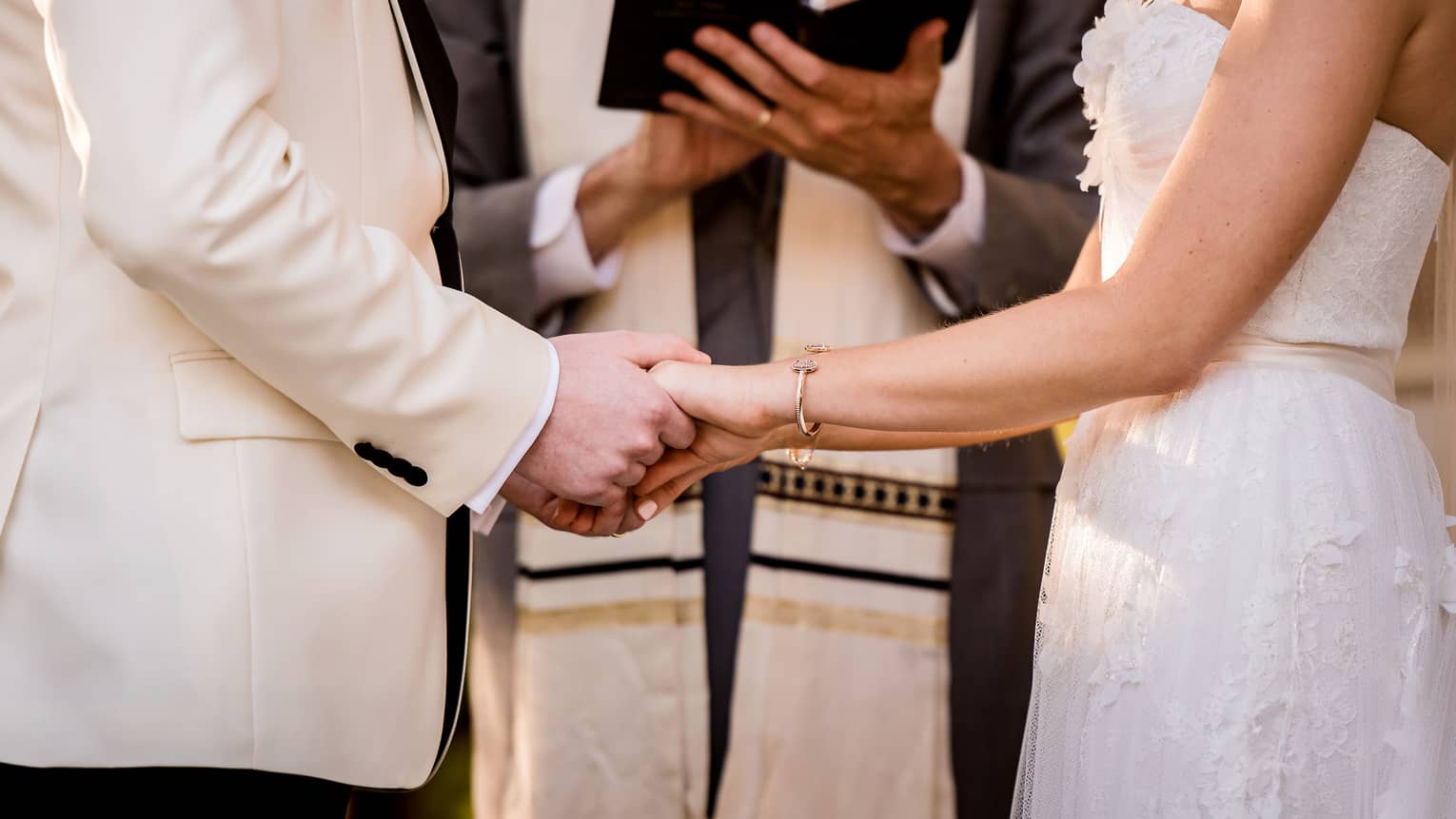 Bride and groom hold hands in front of wedding ceremony officiant