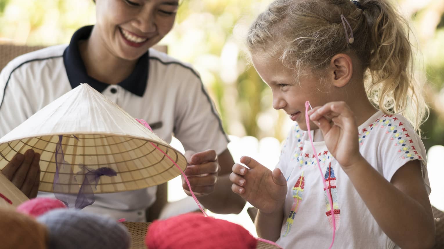 Hotel staff helps young girl thread string on traditional hat