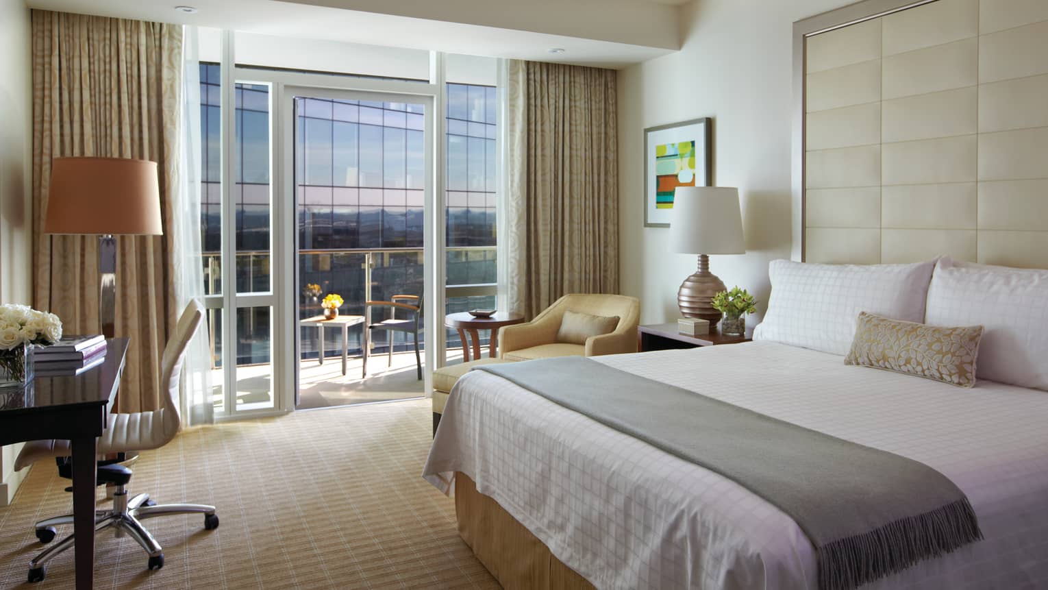 Balcony Room bed with tall headboard, sash, desk, armchair by glass wall, balcony door