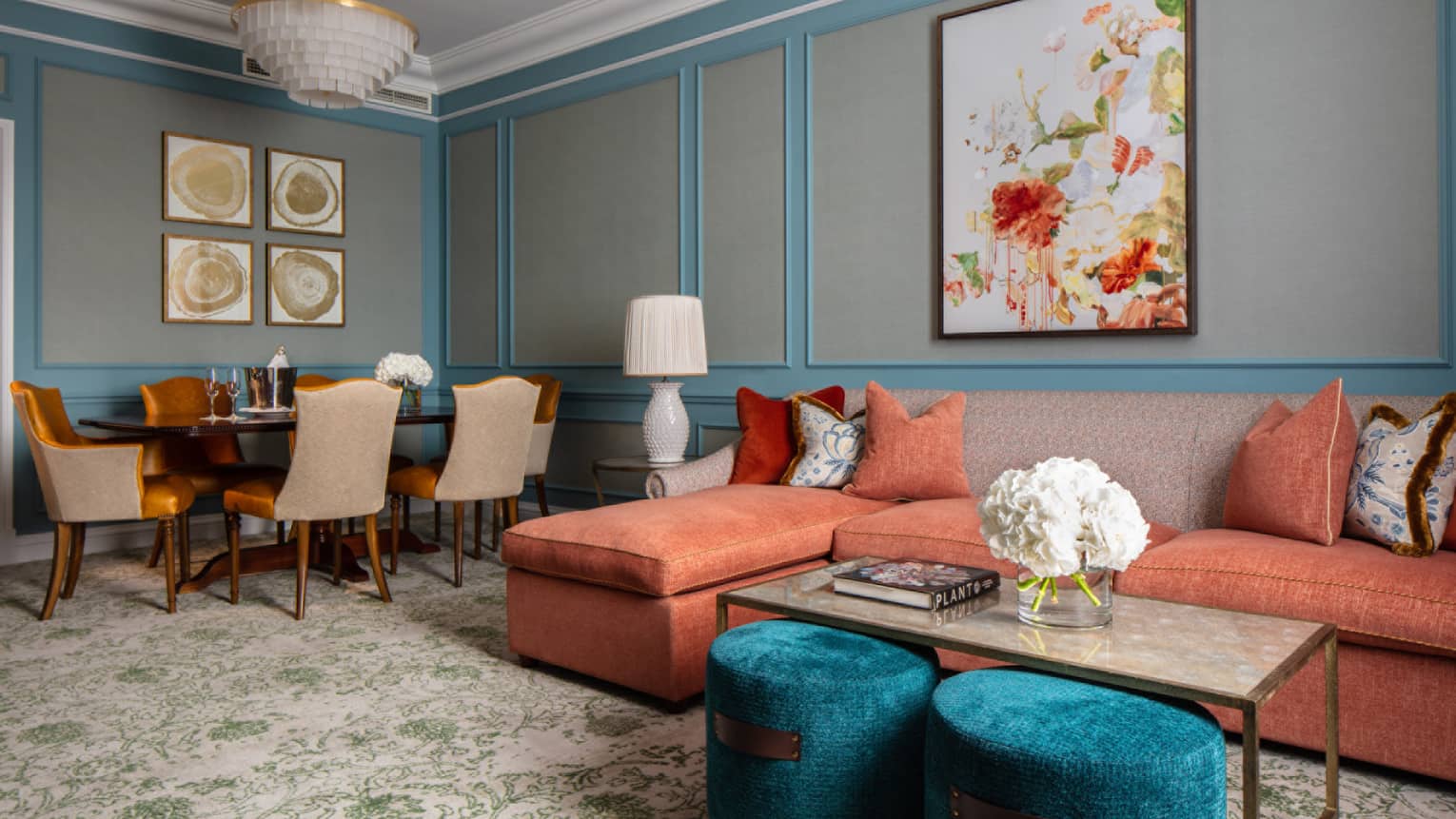 Guest room lounge area with red sectional sofa, coffee table, oblong dining table with six chairs, paisley carpeting, turquoise/grey walls