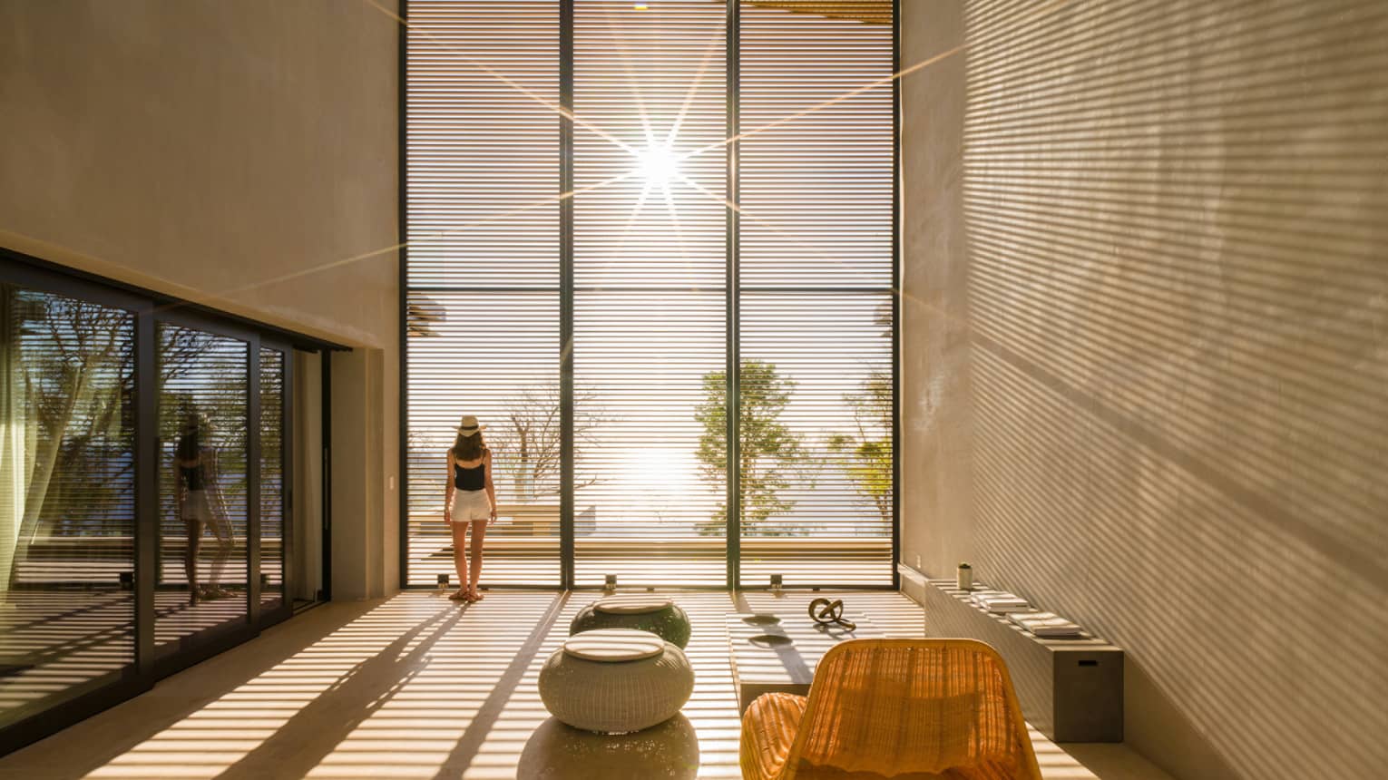 Woman stands by sunny floor to ceiling window in modern room