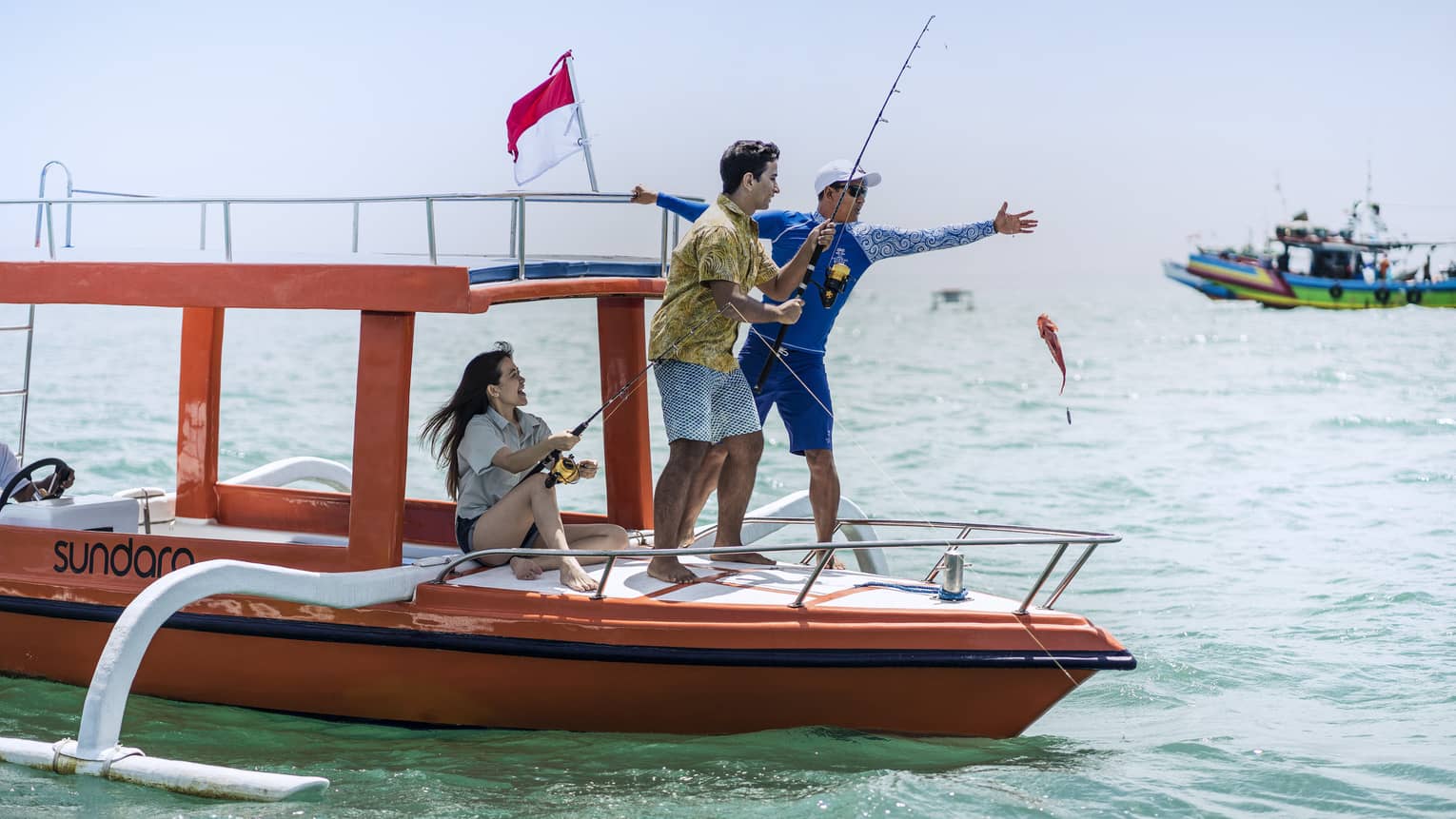 Tour guide teaches two guests to fish on a traditional jukung fishing boat on the open ocean