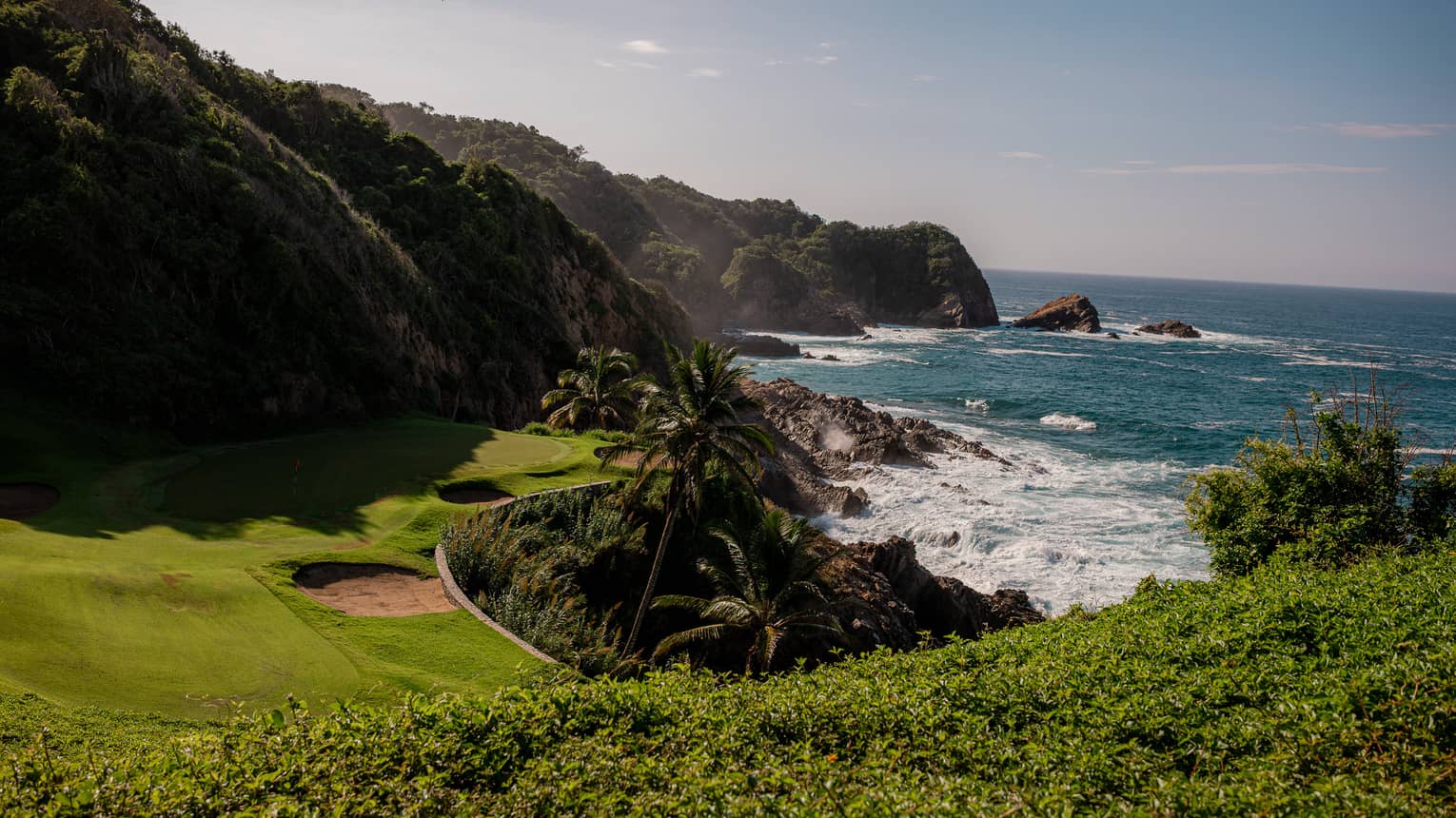 A golf course green nestled between hills and the sea