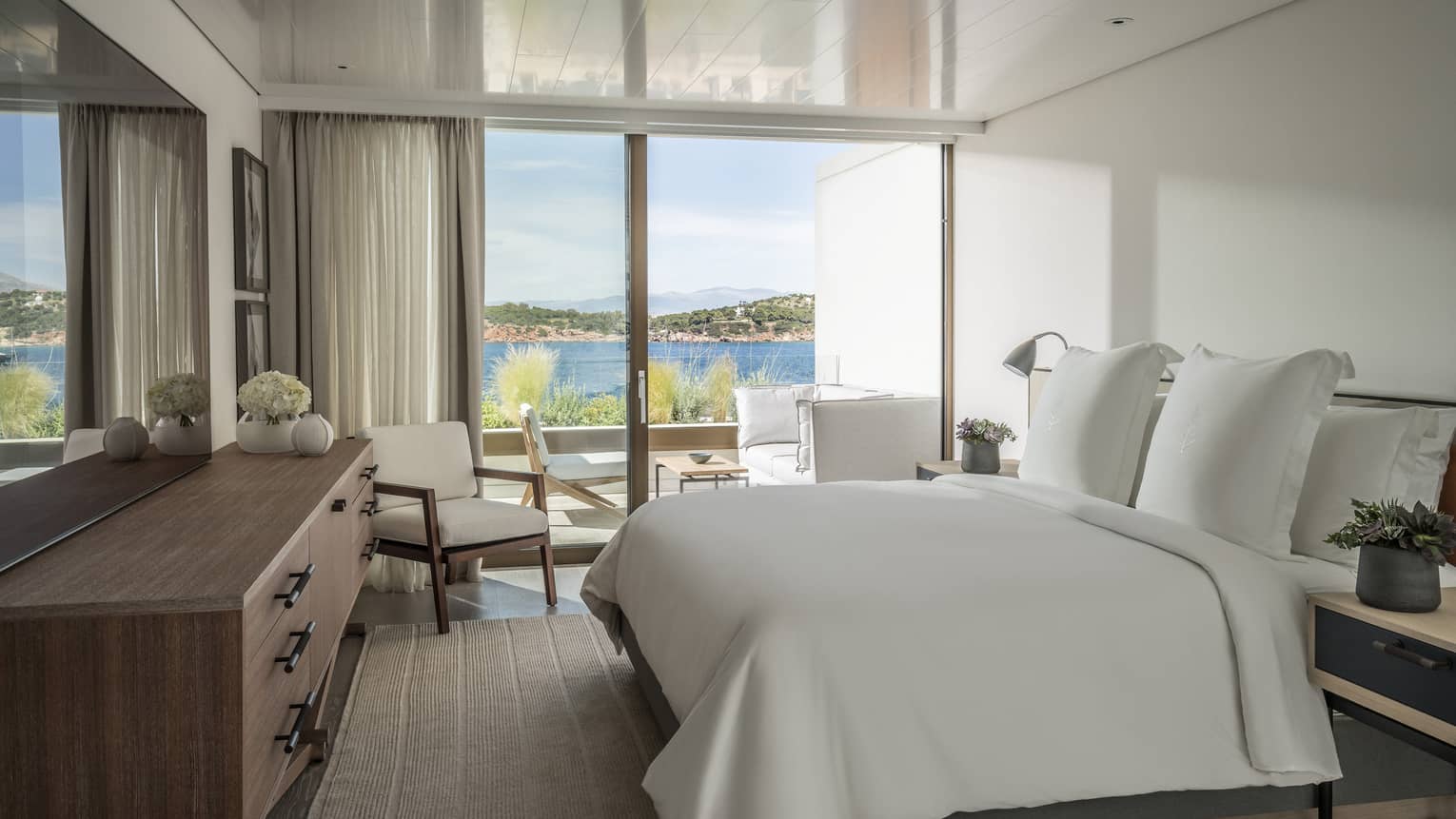 Nafsika Sea View Suite with king bed and white linens, corner arm chair, flat screen TV, sliding glass doors leading to balcony, ocean views