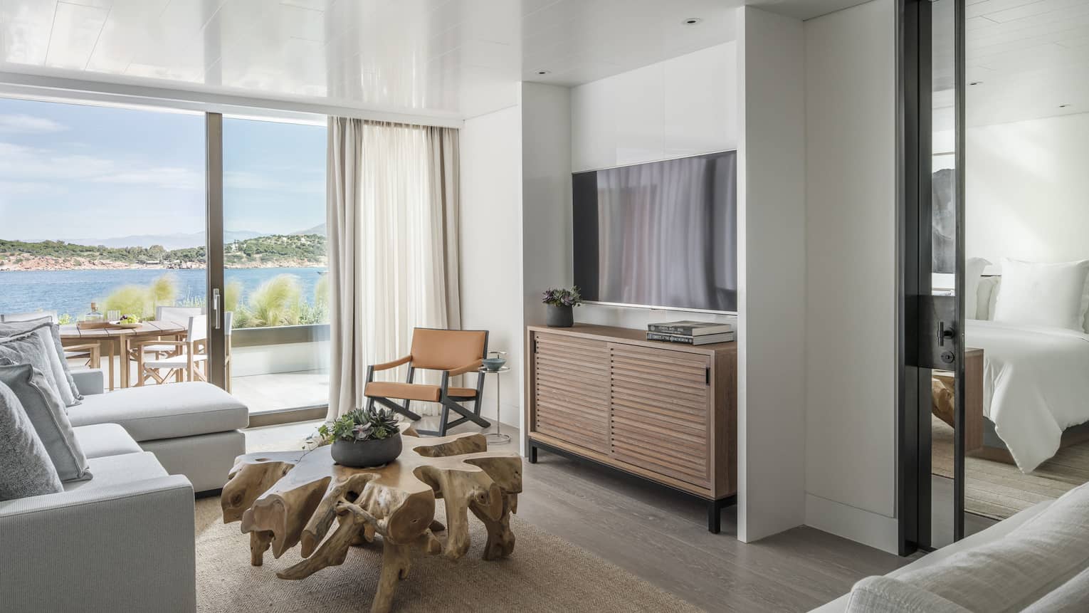 Nafsika Sea View Suite with white sectional sofa, flat screen TV, carved wood coffee table, sliding glass doors opening onto balcony, ocean views