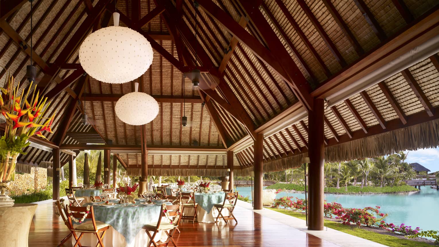 Large globe lanterns over round banquet tables in Otemanu outdoor pavilion by water