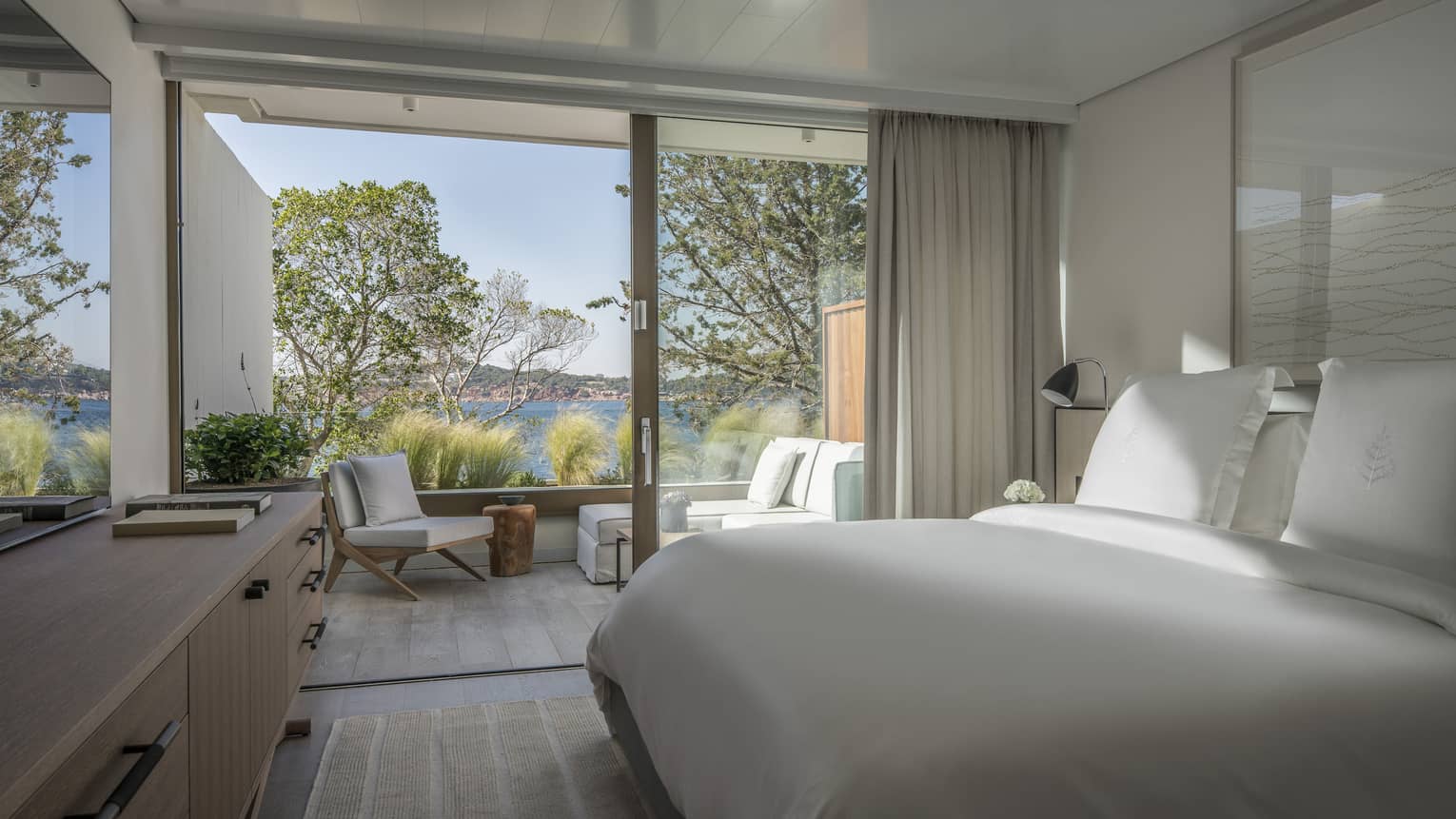 Sleek, Nafsika One Bedroom Terrace Suite with white furniture and bedding overlooking trees and ocean