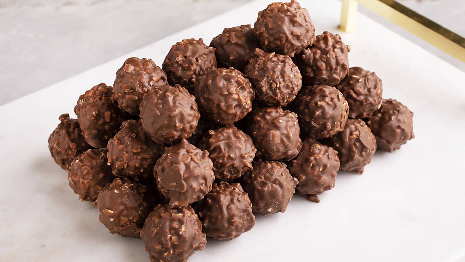 A white plate stacked with truffles featuring a hazelnut anhydrous filling coated with roasted almonds and milk chocolate
