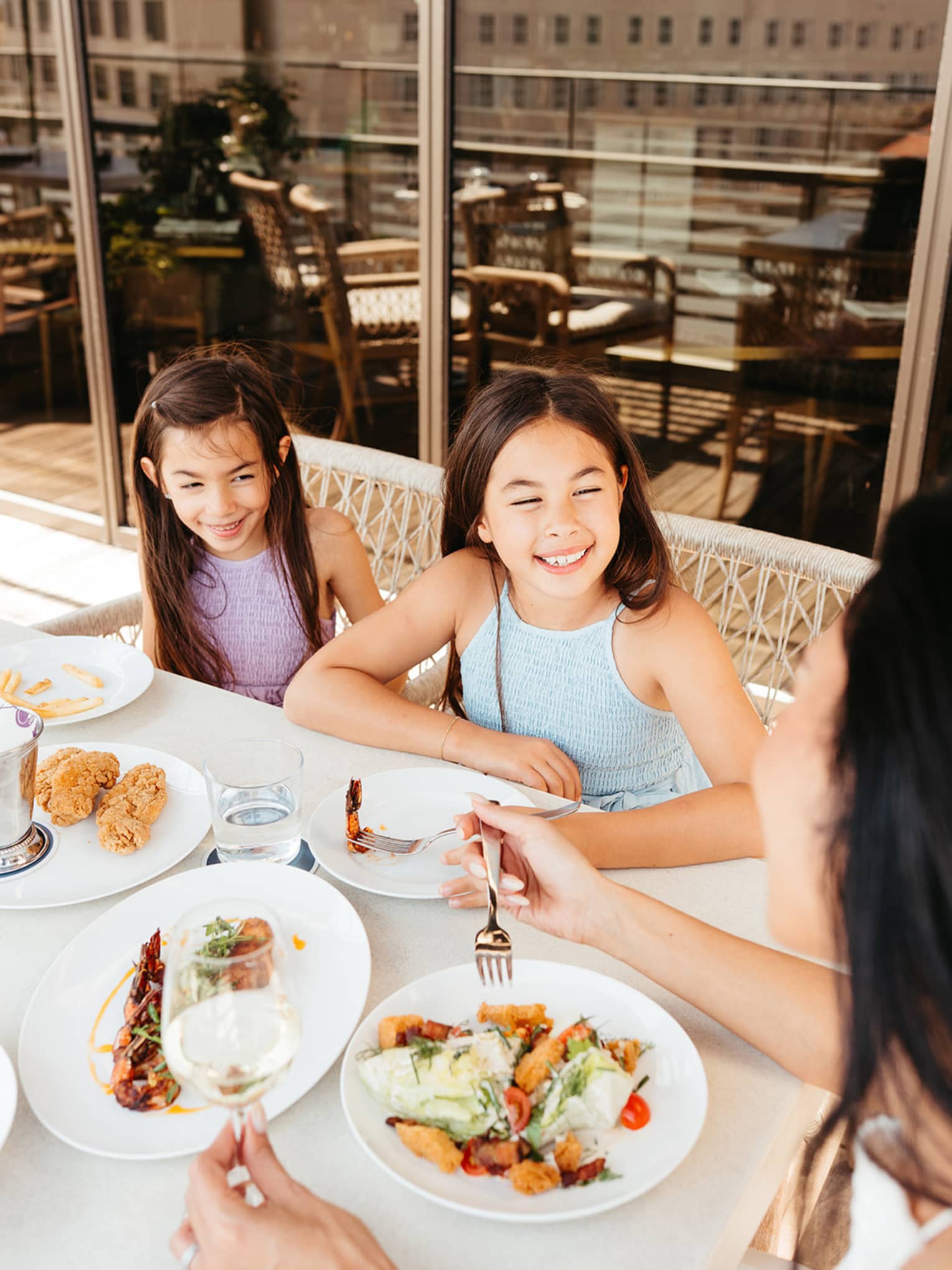 Three guests sitting at an outdoor dining table with floor-to-ceiling windows in the background