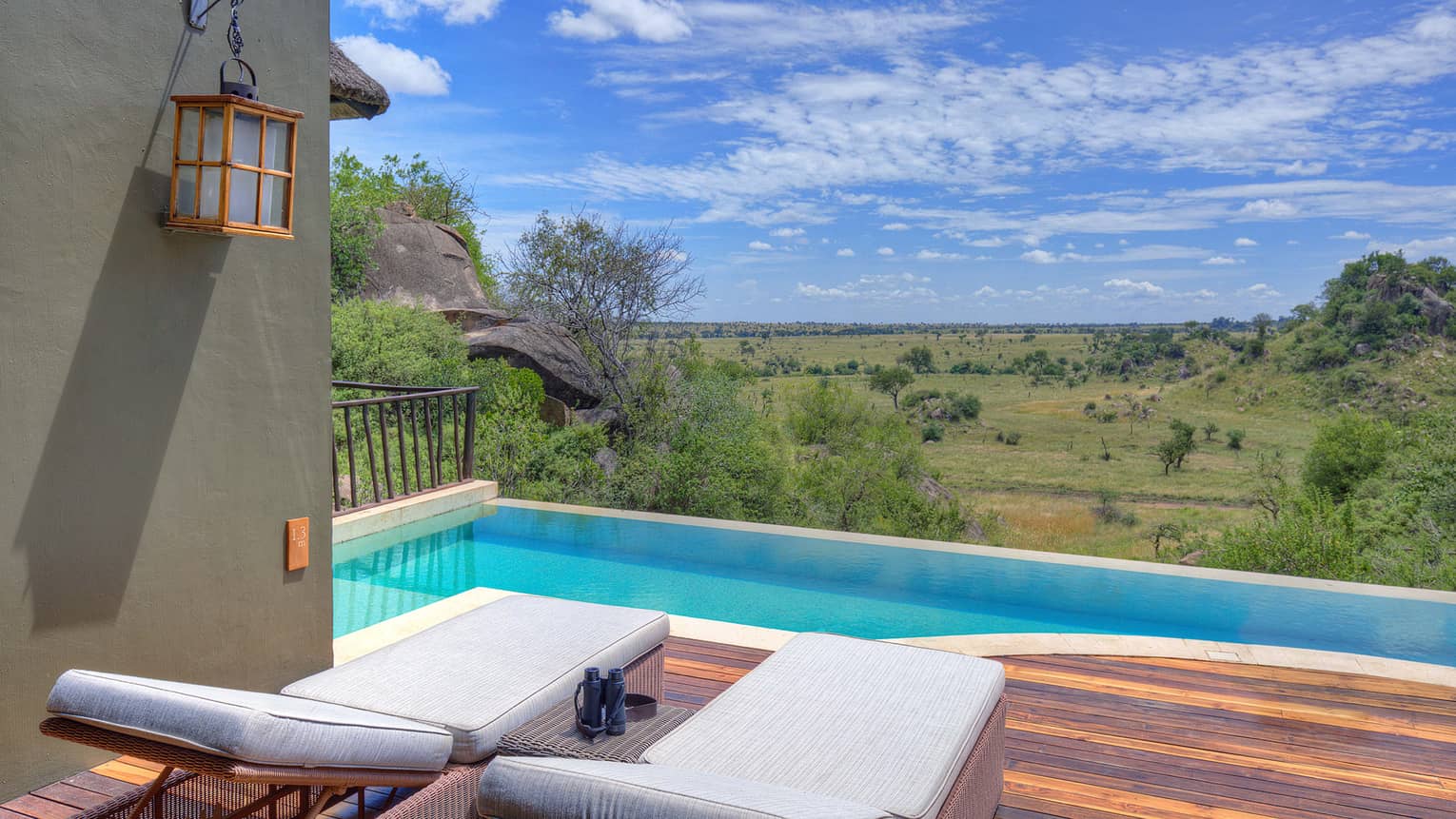 Terrace with two white lounge chairs atop wooden decking beside private pool and with expansive plains under blue sky view