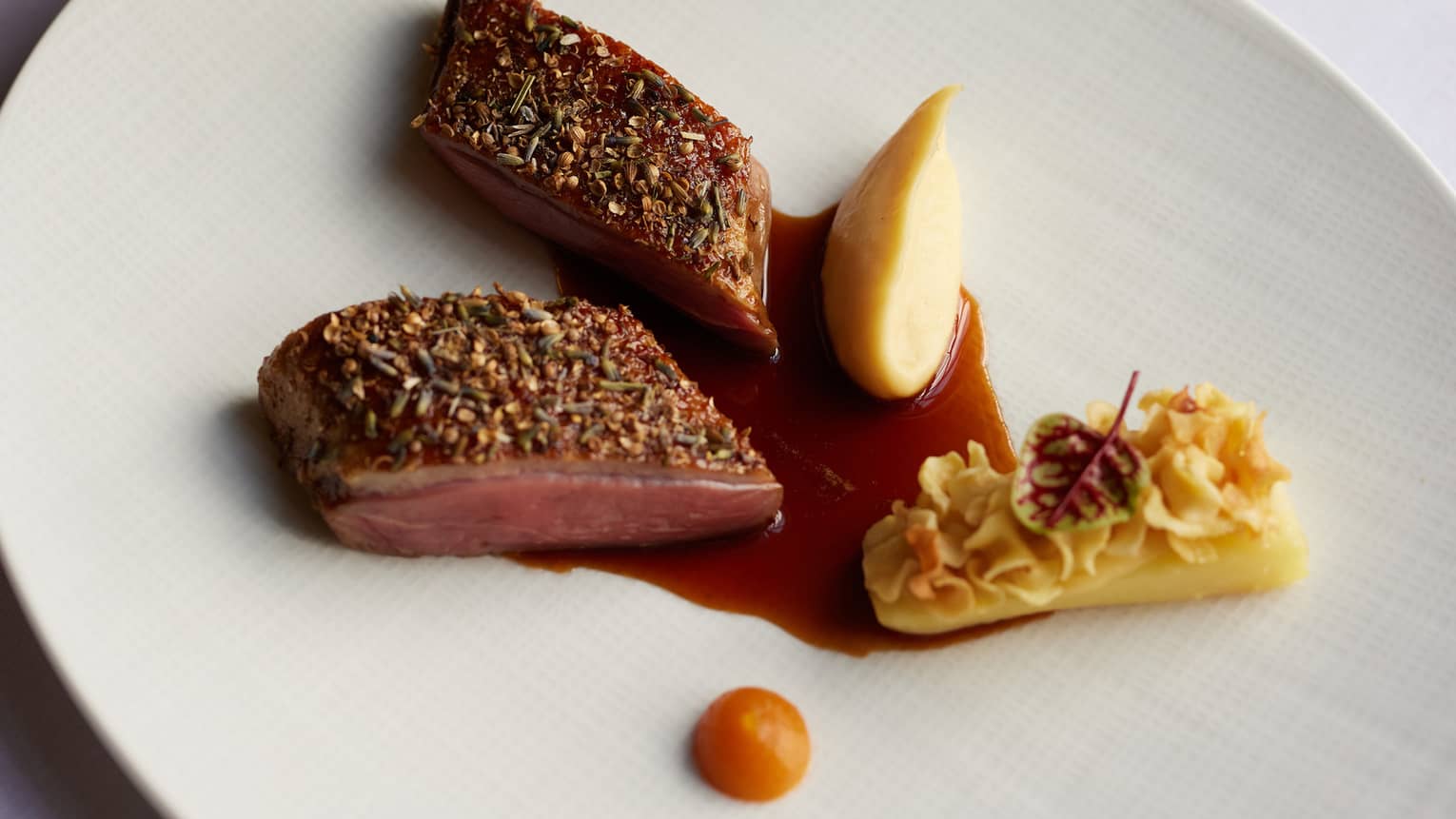 A round white plate holds food items with garnishes and a sauce.
