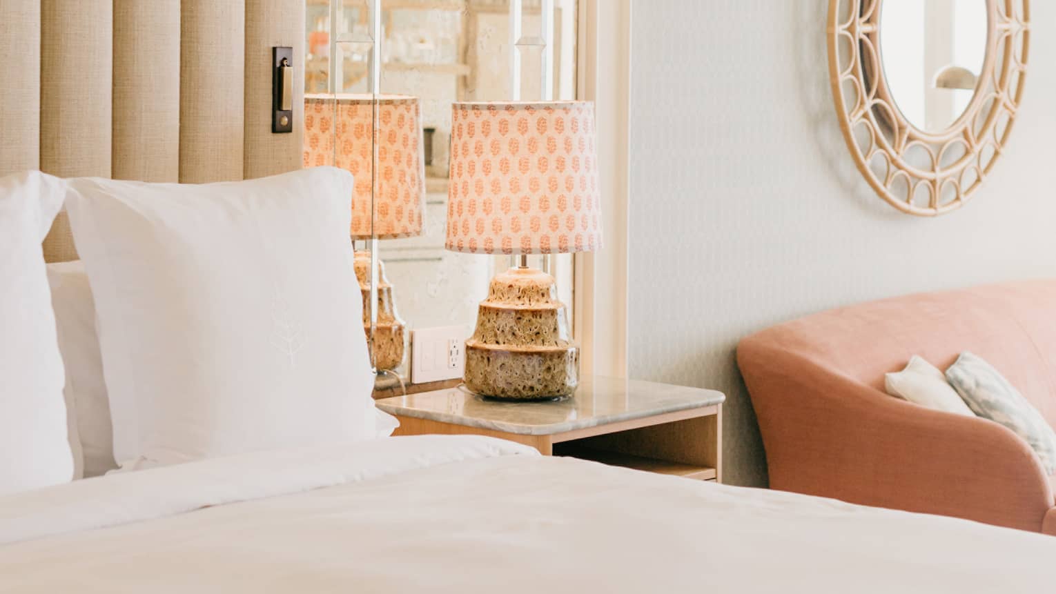 Elegant hotel room with a plush white bed, mirrored headboard, stylish lamps on nightstands, and a round decorative mirror on the wall. 