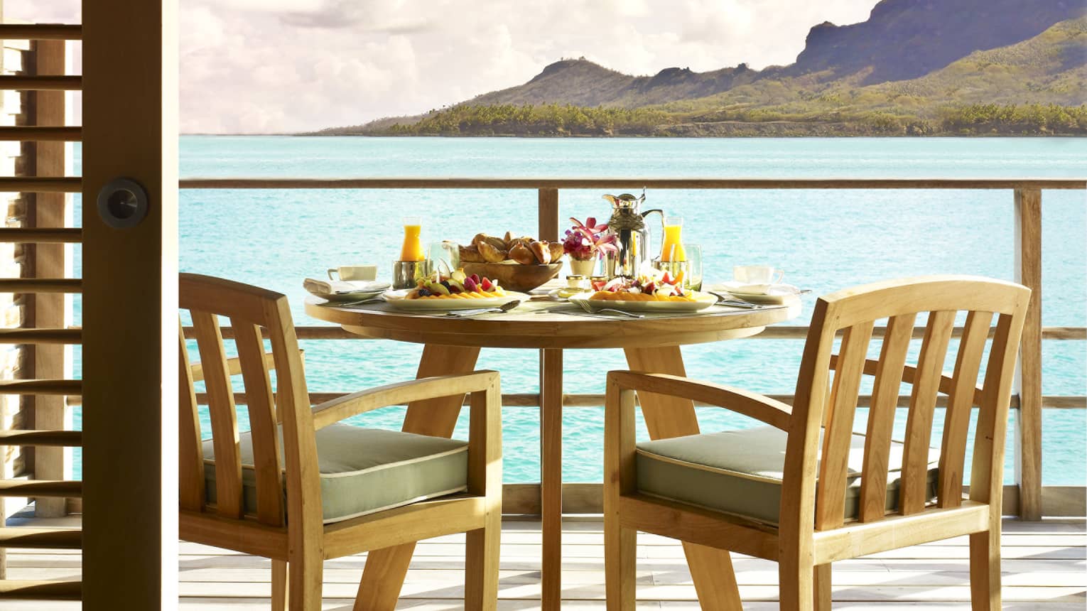 Private in-bungalow dining table with fresh fruit and breakfast plates overlooking lagoon and mountains